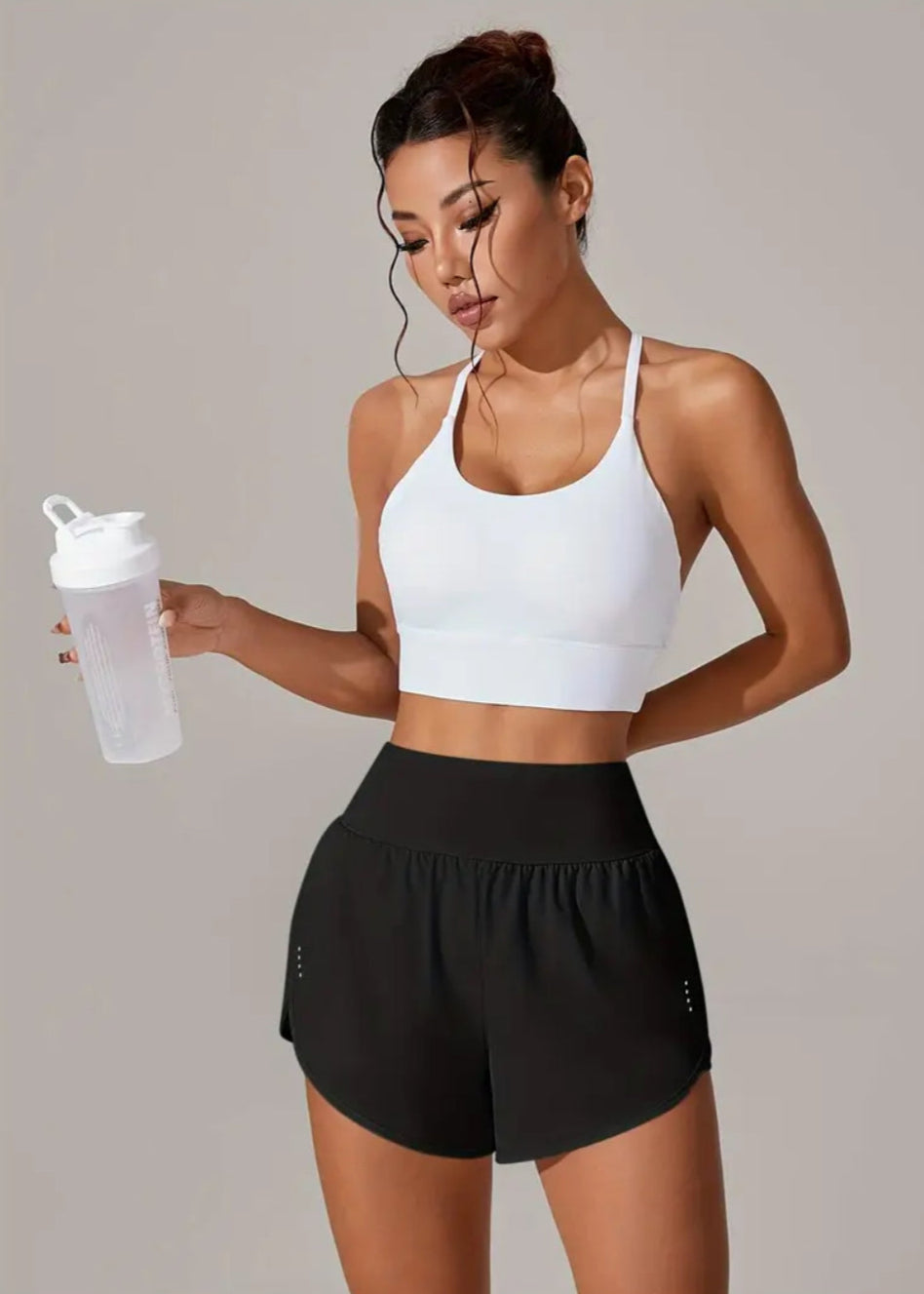 Woman in athletic wear holding a water bottle against a plain background