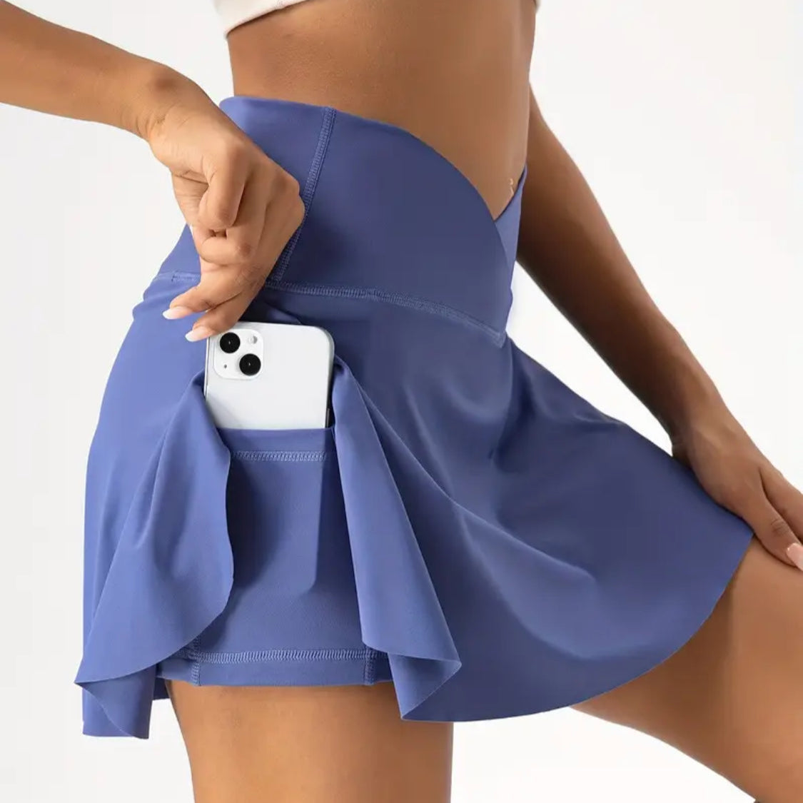Person wearing a blue skirt with a white phone case visible through the pocket on a plain background