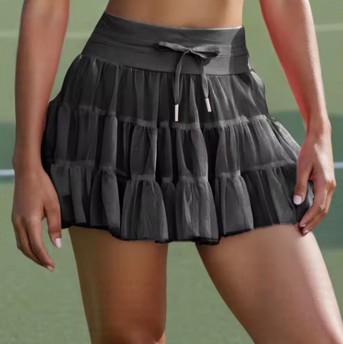 Person wearing a black tiered skirt and pink top on a tennis court.