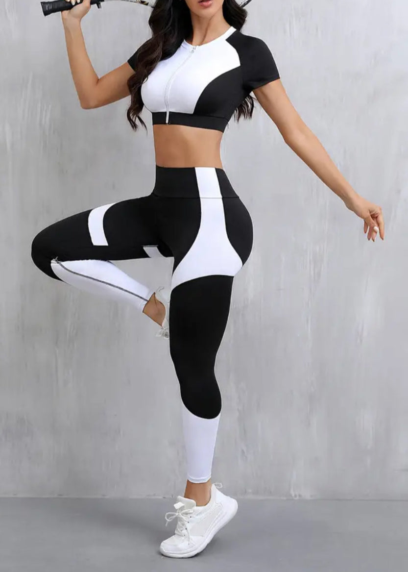 Woman in black and white athletic wear posing with a tennis racket against a gray background
