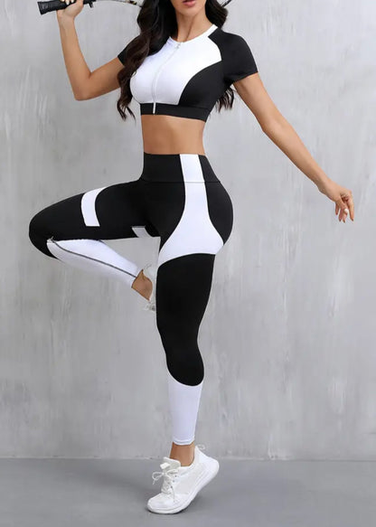 Woman in black and white athletic wear posing with a tennis racket against a gray background