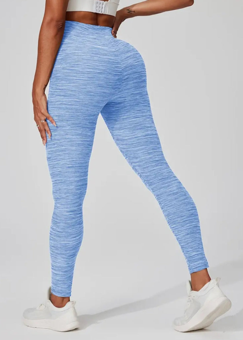 A pair of blue Yoga Space Dye Leggings featuring a high-rise waistband and a no front seam design, modeled by a person posing with one hand on her hip.