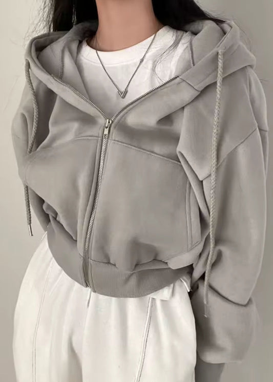 Person wearing a gray zip-up hoodie over a white shirt and pants on a plain background