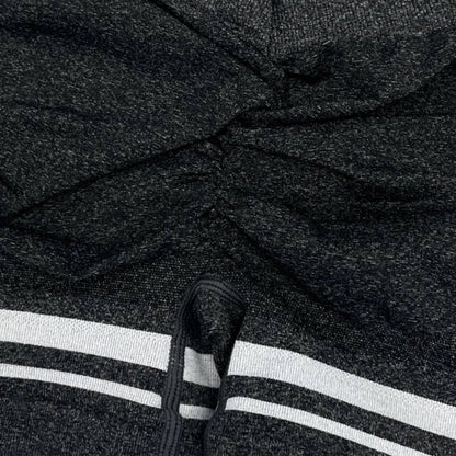 Close-up of a dark gray hoodie with white stripes on the sleeve, worn by a person.
