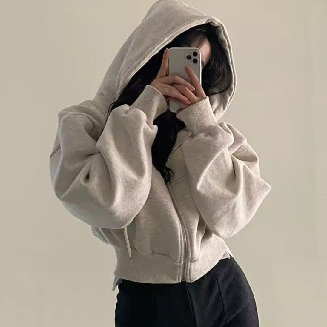 Person wearing a beige hoodie holding a phone on a plain background